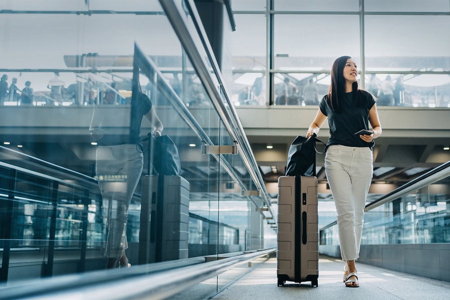 Young Asian woman with passport carrying suitcase walking in the airport concourse